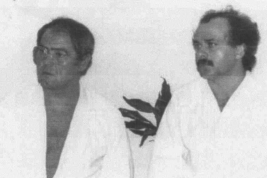 Schwarz-Weiss-Foto von zwei Männern in weissen Keikogi, der eine mit Brille, der andere mit Schnurrbart und lockigem Haar.